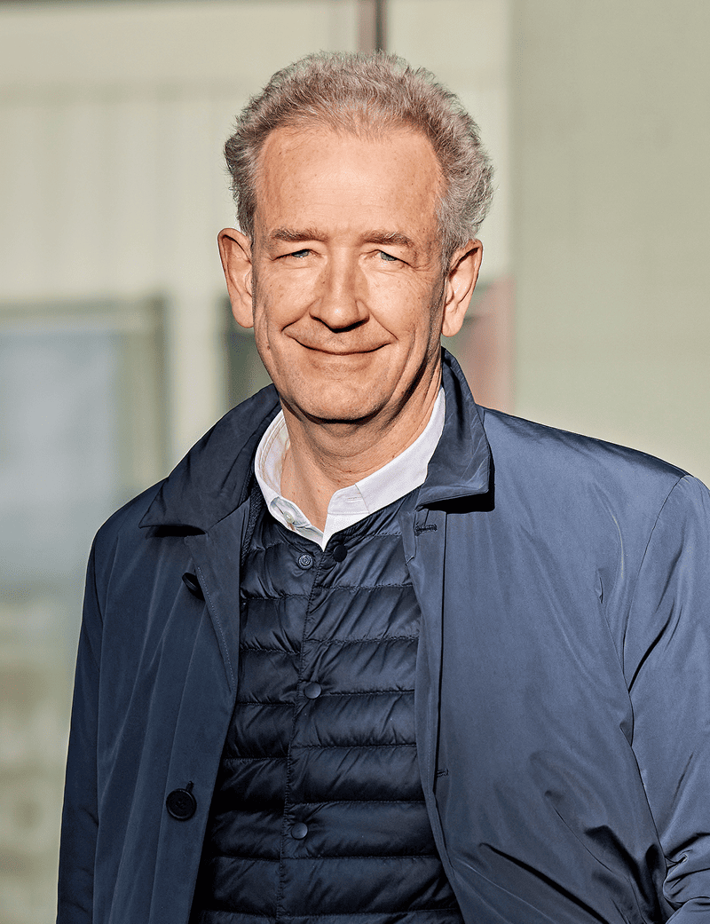 Uomo in piedi con giacca blu, sorridente: Adrian Bult
